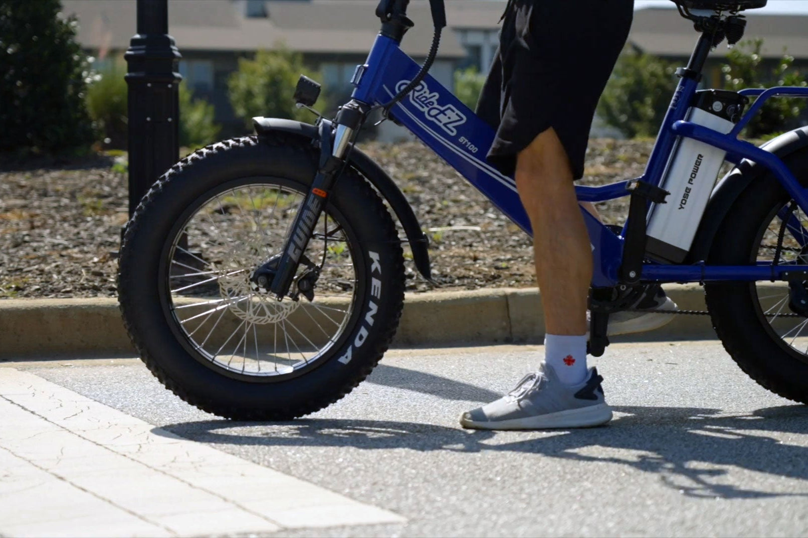 Person riding a blue electric bike on a sidewalk